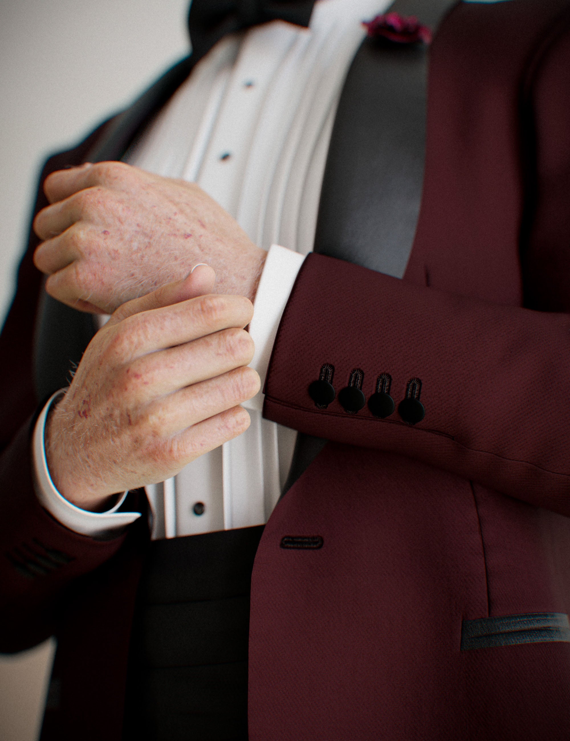 Close-up of Genesis 9 male tuxedo sleeve, cuff buttons, shirt pleats, and burgundy jacket fabric